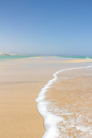 View looking down a long beach while the waves crash on the shore with a kayaker in the distance.  